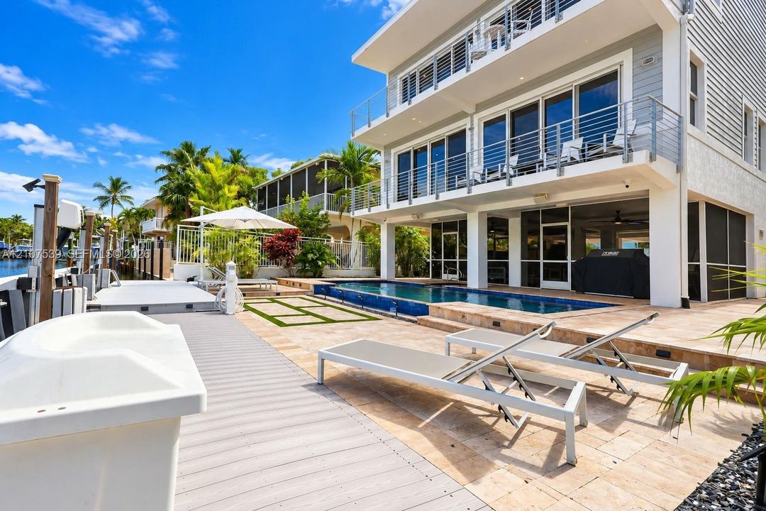 Three-story waterfront residence featuring a multi-level balcony system with cable railings, a private in-ground swimming pool, stone-paver hardscaping, and a synthetic deck area with a boat dock