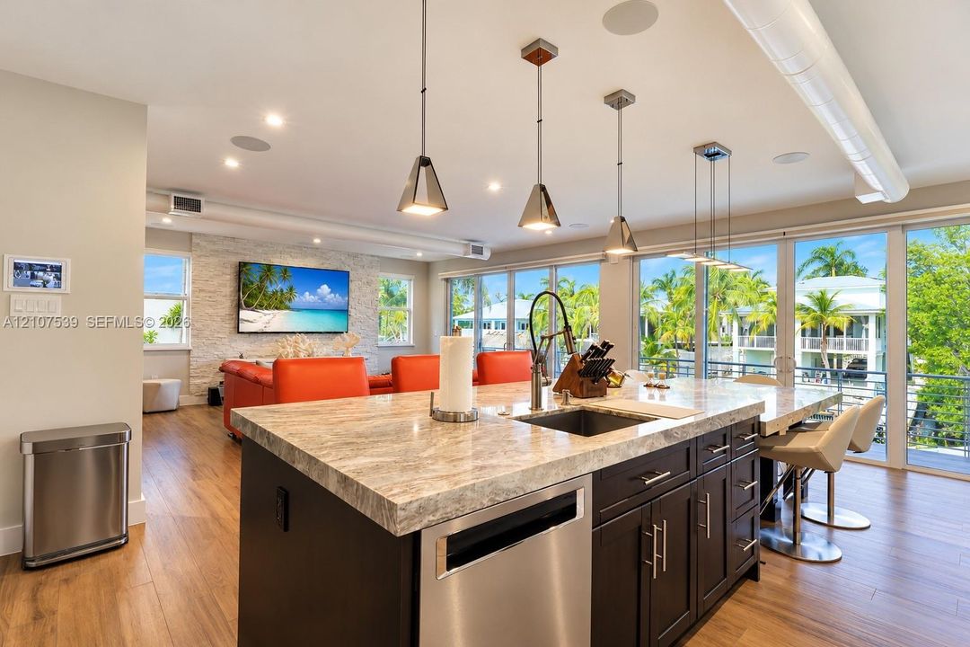 Center island with stone countertop, dark cabinetry, stainless steel dishwasher, recessed lighting, and metal pendant fixtures