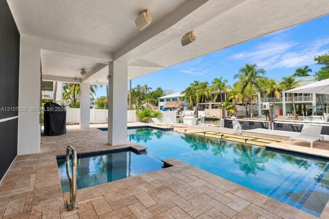 Covered lanai with stone-paver decking, swimming pool featuring an integrated spa, and concrete bulkhead leading to a waterway