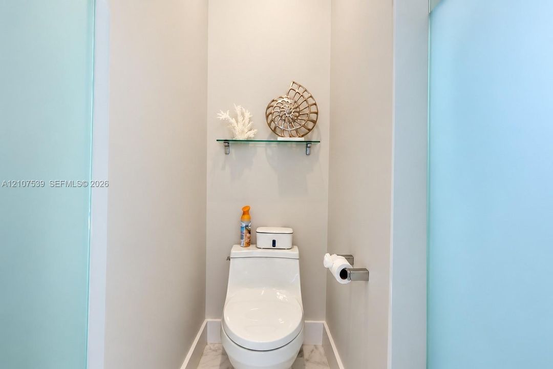 Wall-mounted glass shelving, one-piece dual-flush toilet, and frosted glass privacy panels