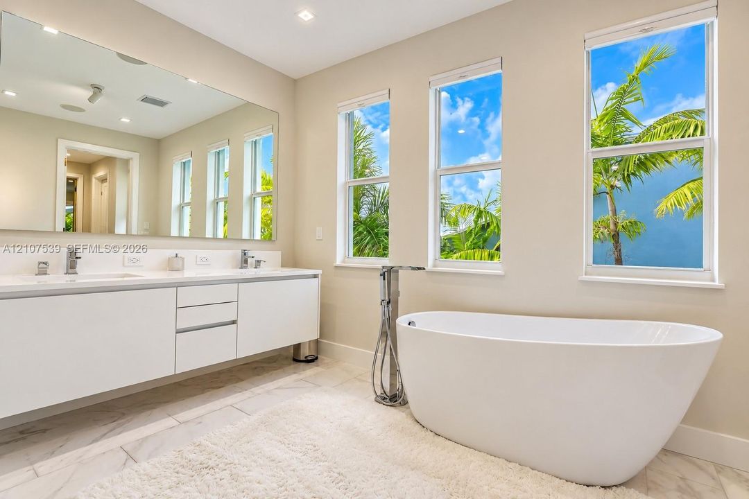 Floating vanity with dual rectangular sinks, oversized frameless wall mirror, freestanding soaking tub, chrome floor-mounted tub filler, and tile flooring