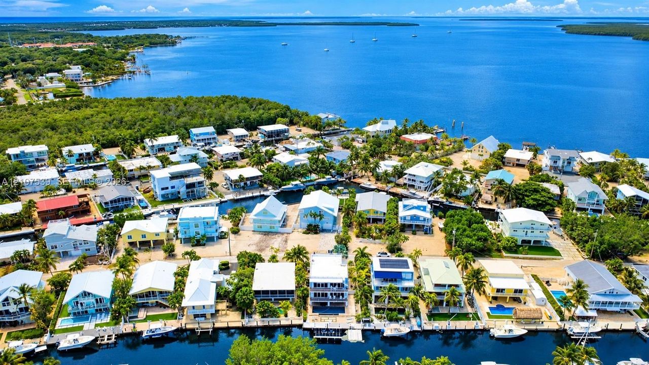 Aerial perspective of a coastal residential community featuring deep-water canal access, private boat docks, and surrounding open water