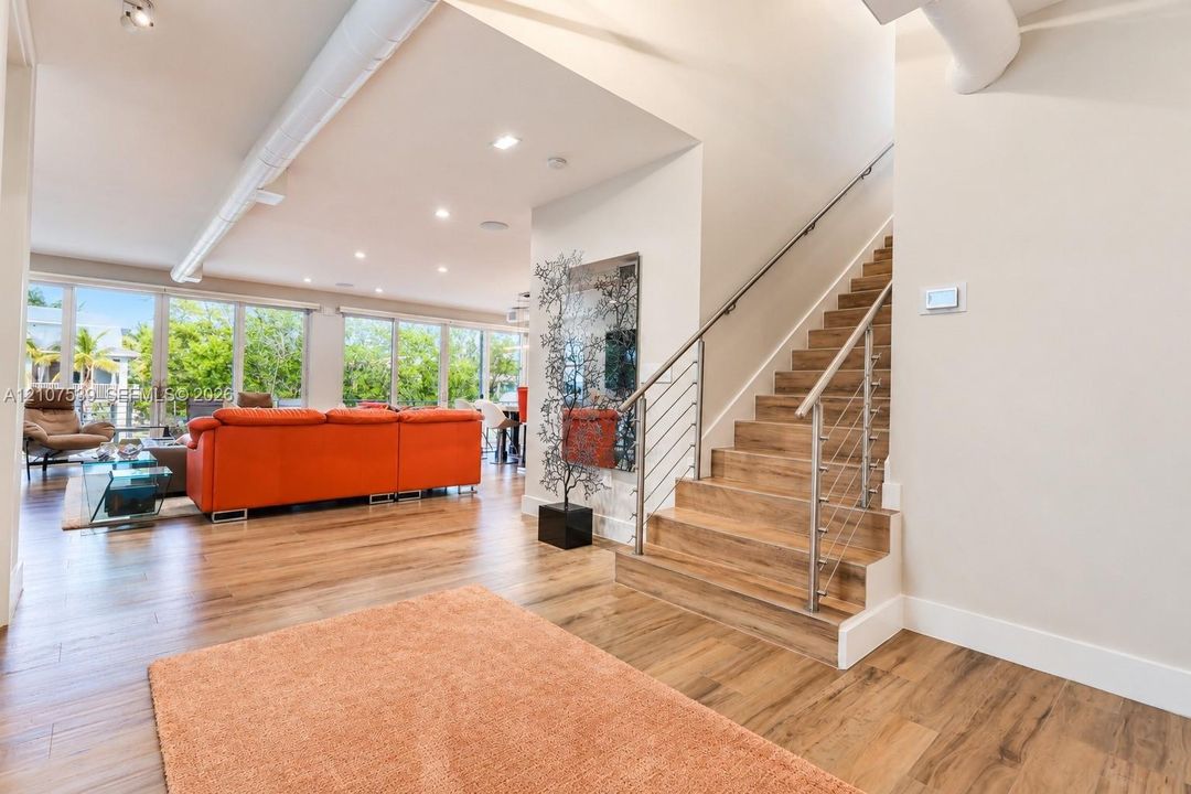 Open floor plan featuring wood-finish flooring, floor-to-ceiling windows, exposed industrial ductwork, recessed lighting, and a staircase with cable railings and wood-finish treads