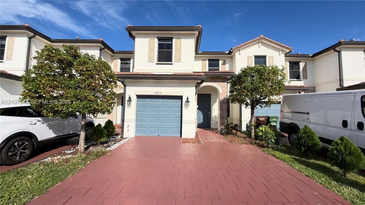 Two-story townhouse exterior featuring light-toned stucco siding, a paved driveway, and an integrated single-car garage with a paneled door