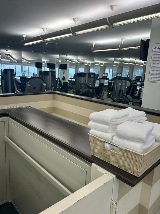 Fitness area featuring full-wall mirrors, recessed lighting, and a built-in service counter with a dark wood-finish top