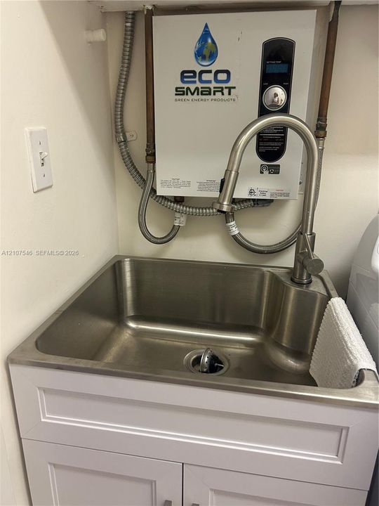 Stainless steel utility sink featuring a high-arc pull-down faucet, mounted above a white shaker-style vanity cabinet, accompanied by an electric tankless water heater