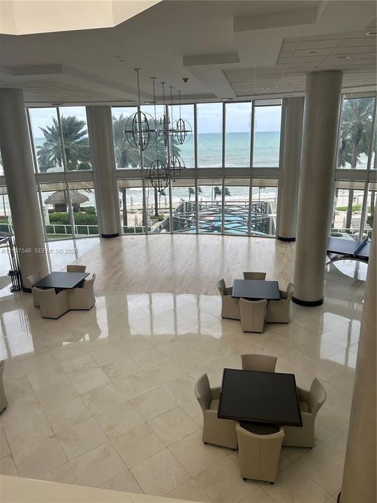 Double-height floor-to-ceiling windows, polished tile flooring, wood-finish flooring accents, structural cylindrical columns, and metal orb pendant lighting