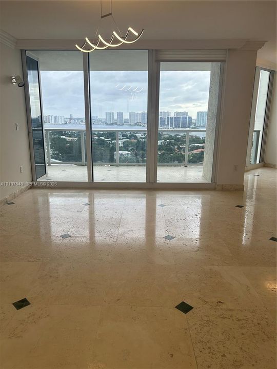 Polished stone flooring with decorative inlays, expansive floor-to-ceiling glass sliding doors, private balcony, contemporary geometric pendant lighting, and panoramic water and city skyline outlooks