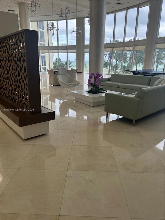 Grand lobby featuring floor-to-ceiling windows, polished stone flooring, custom decorative wood partition, and spherical pendant lighting