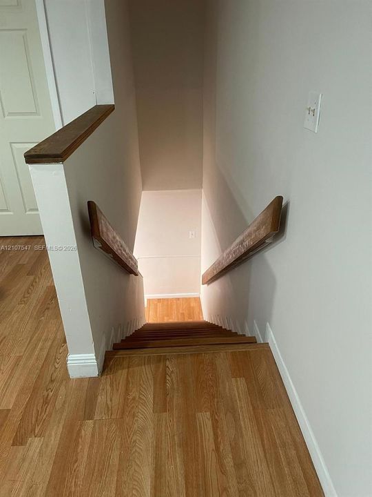 Staircase featuring wood-finish flooring, wood handrails, and a half-wall with a wood-finish cap