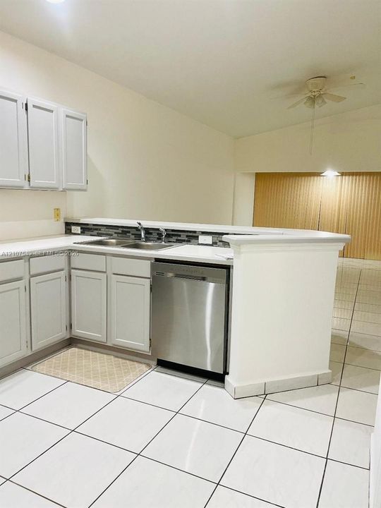 Kitchen featuring white shaker-style cabinetry, stainless steel dishwasher, dual-basin stainless steel sink, tiled backsplash, and white tile flooring
