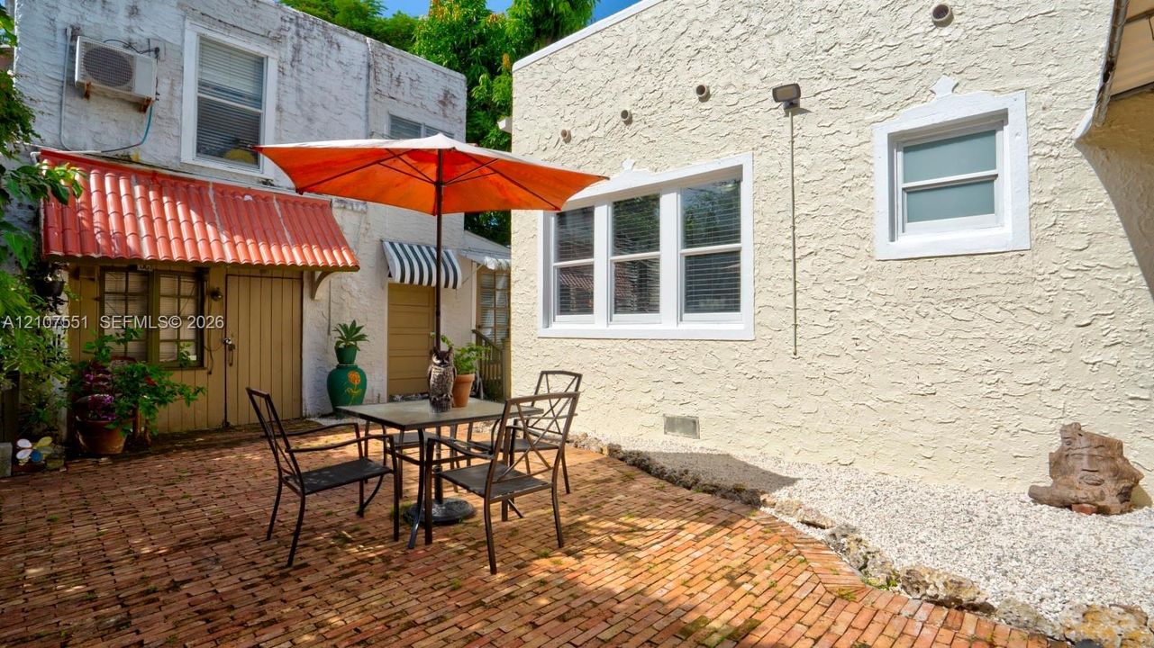 Enclosed courtyard featuring a red brick patio, textured stucco exterior walls, multi-pane windows, and a terracotta-style awning