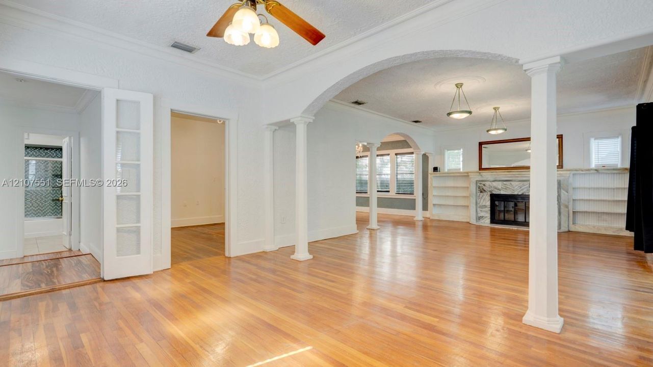 Interior space featuring architectural columns, arched entryways, wood-finish flooring, a fireplace with stone surround, and built-in shelving