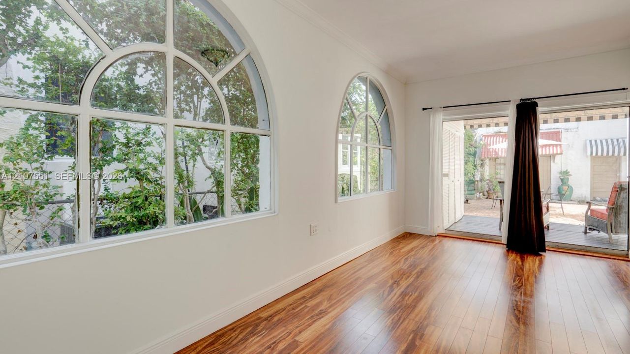 Wood-finish flooring, large arched windows, and a sliding glass door providing access to an outdoor patio