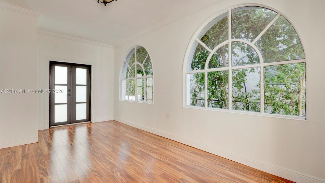 Wood-finish flooring, two large arched windows with muntins, and a dark-framed entry door with frosted glass panes