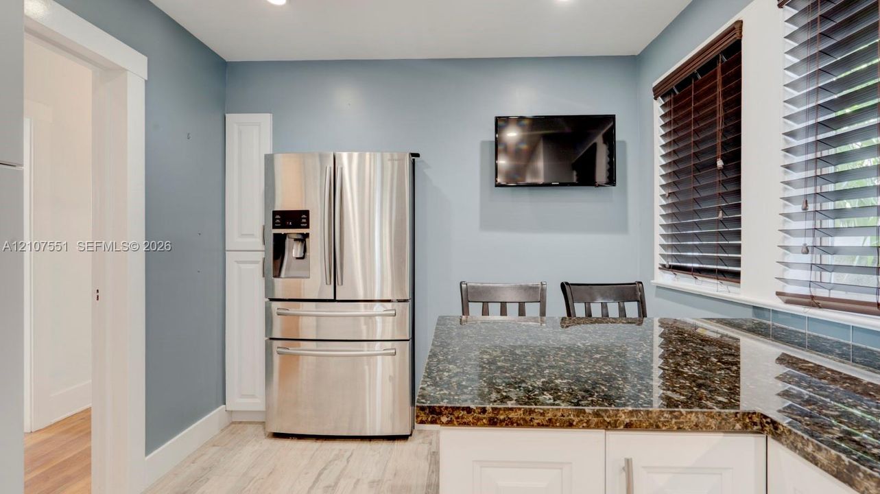 Kitchen featuring stone countertops, white shaker-style cabinetry, stainless steel French-door refrigerator, wood-finish flooring, and horizontal window blinds