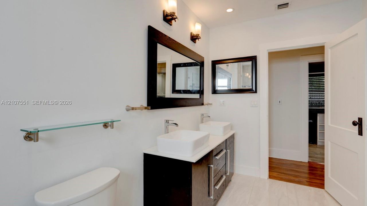 Double vanity featuring rectangular vessel sinks, quartz countertops, dark-toned cabinetry, polished metal hardware, and dual wall-mounted mirrors