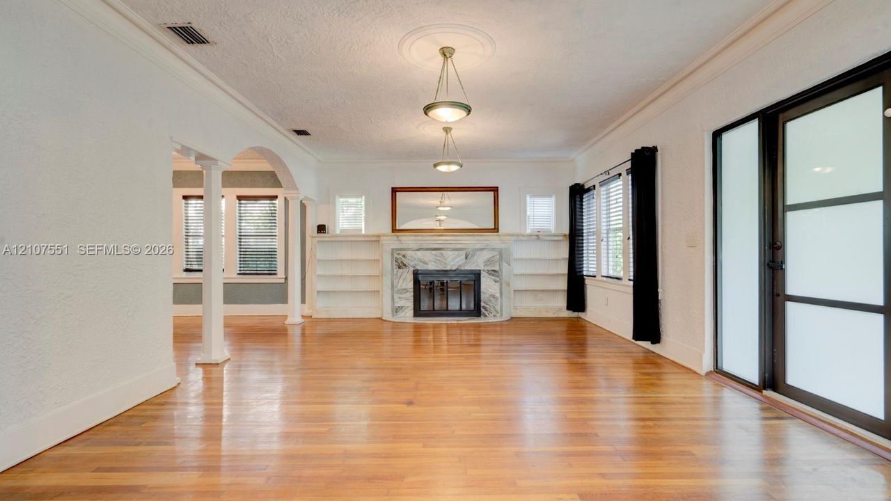 Living area featuring wood-finish flooring, a stone-surround fireplace with built-in shelving, two hanging pendant lights with ceiling medallions, and structural columns