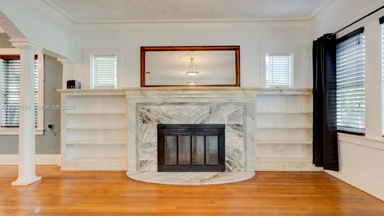 Fireplace featuring a stone surround and hearth, flanked by symmetrical built-in shelving, complemented by wood-finish flooring and crown molding