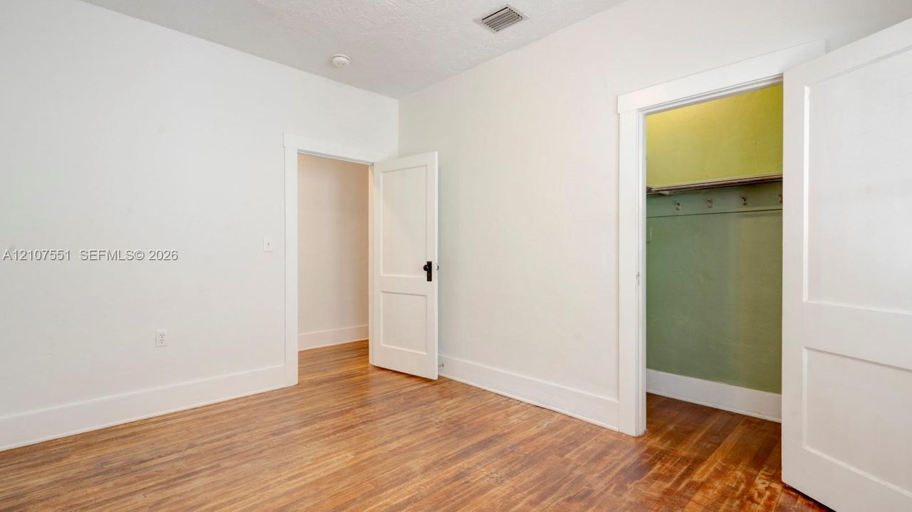 Neutral-toned interior space featuring wood-finish flooring, two-panel interior doors with matte black hardware, and an open storage area with integrated shelving