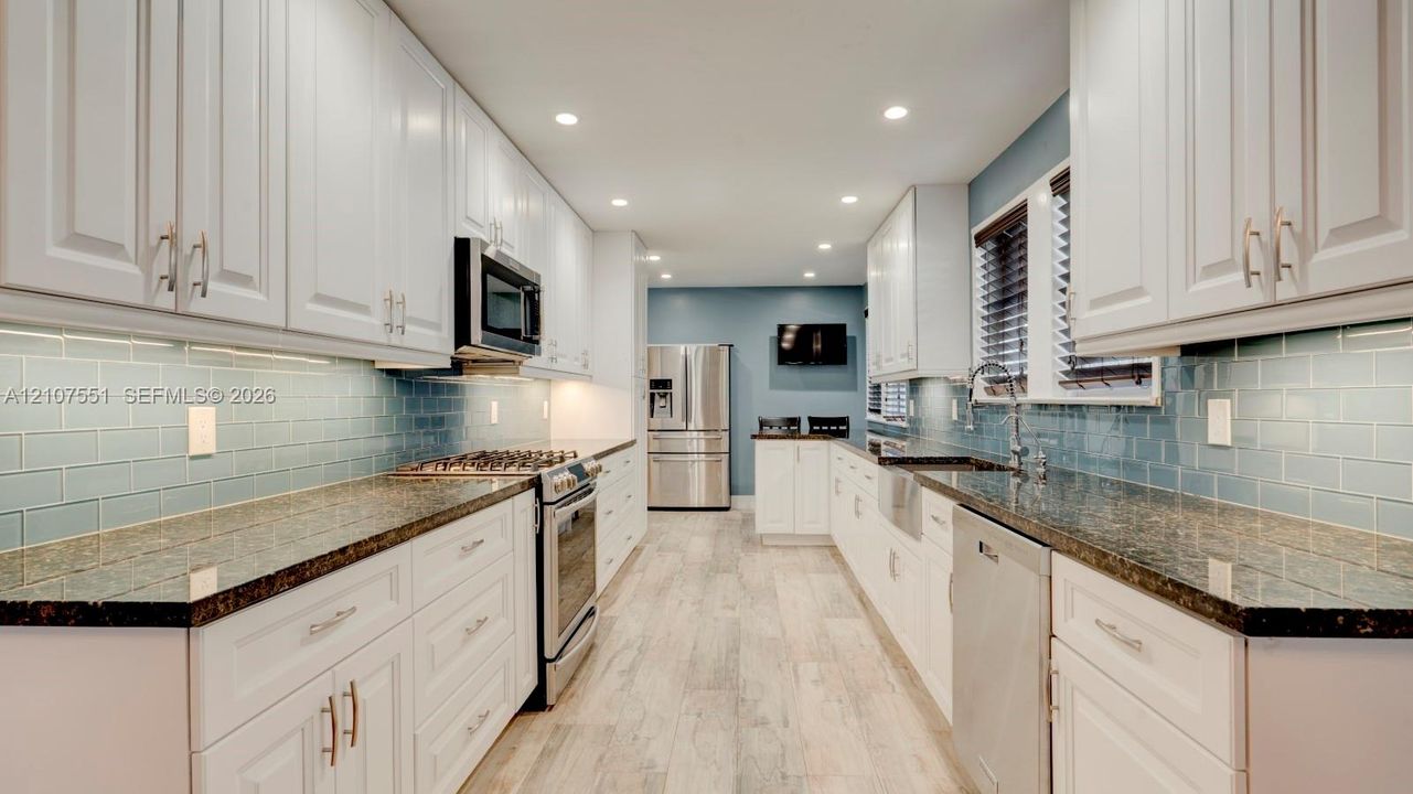 Kitchen featuring shaker-style white cabinetry, dark stone countertops, blue subway tile backsplash, stainless steel appliances, and wood-finish flooring