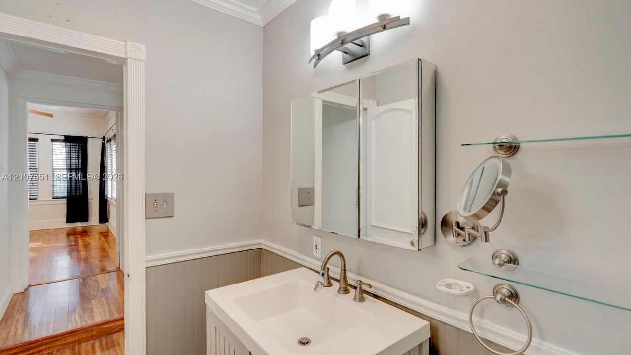 Vanity featuring a rectangular basin, metallic faucet, mirrored medicine cabinet, wall-mounted glass shelving, and beadboard wainscoting