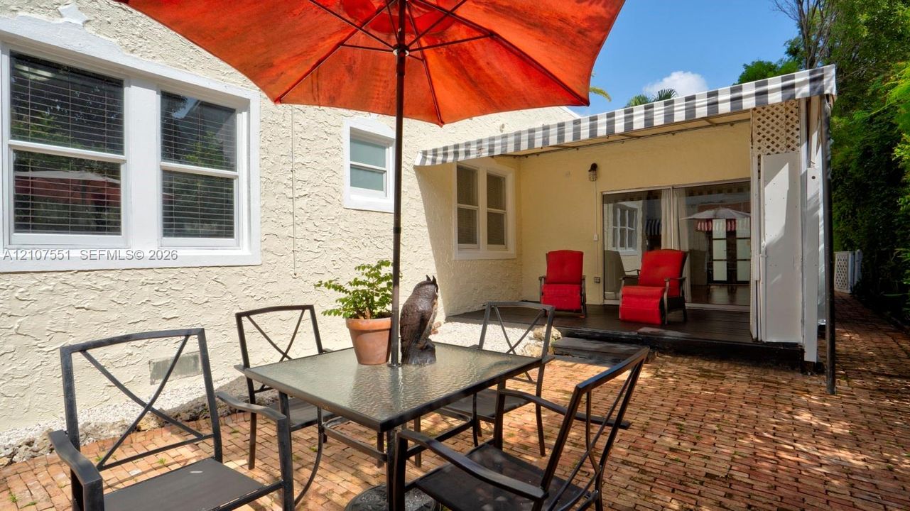 Stucco exterior featuring a brick-paved patio, retractable striped awning, and large white-trimmed windows