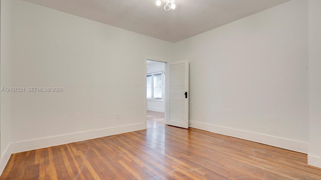 Room interior featuring wood-finish flooring, a white five-panel interior door with a black hardware set, and a ceiling-mounted light fixture