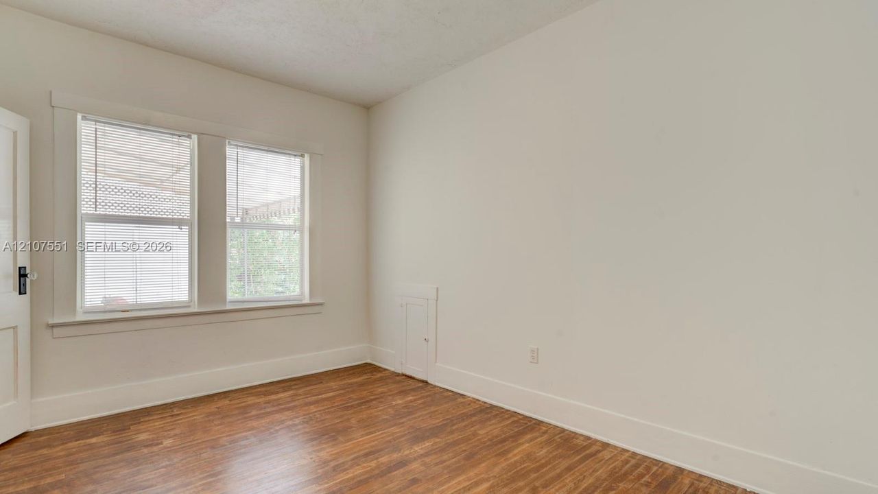 Interior room featuring wood-finish flooring, dual windows with decorative millwork casing, and a built-in wall access panel