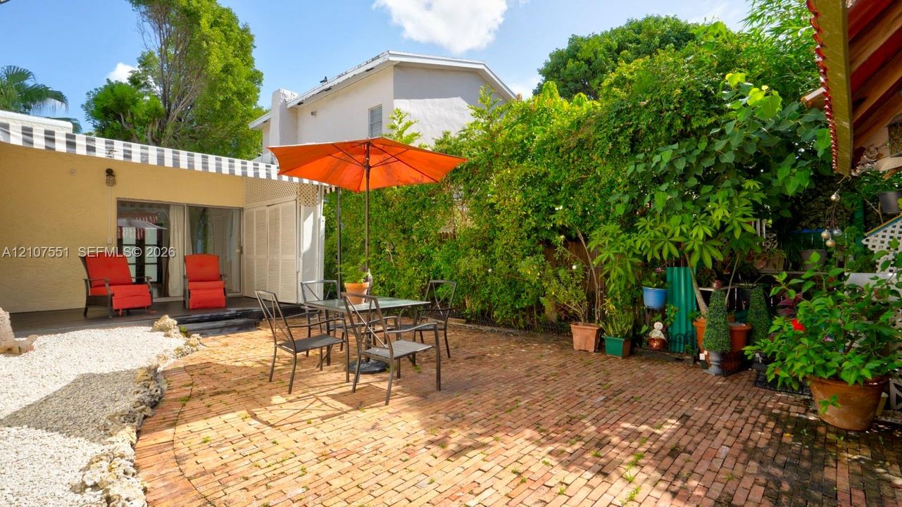 Rear patio featuring a brick-paved surface, a black-and-white striped fixed awning, and natural foliage screening