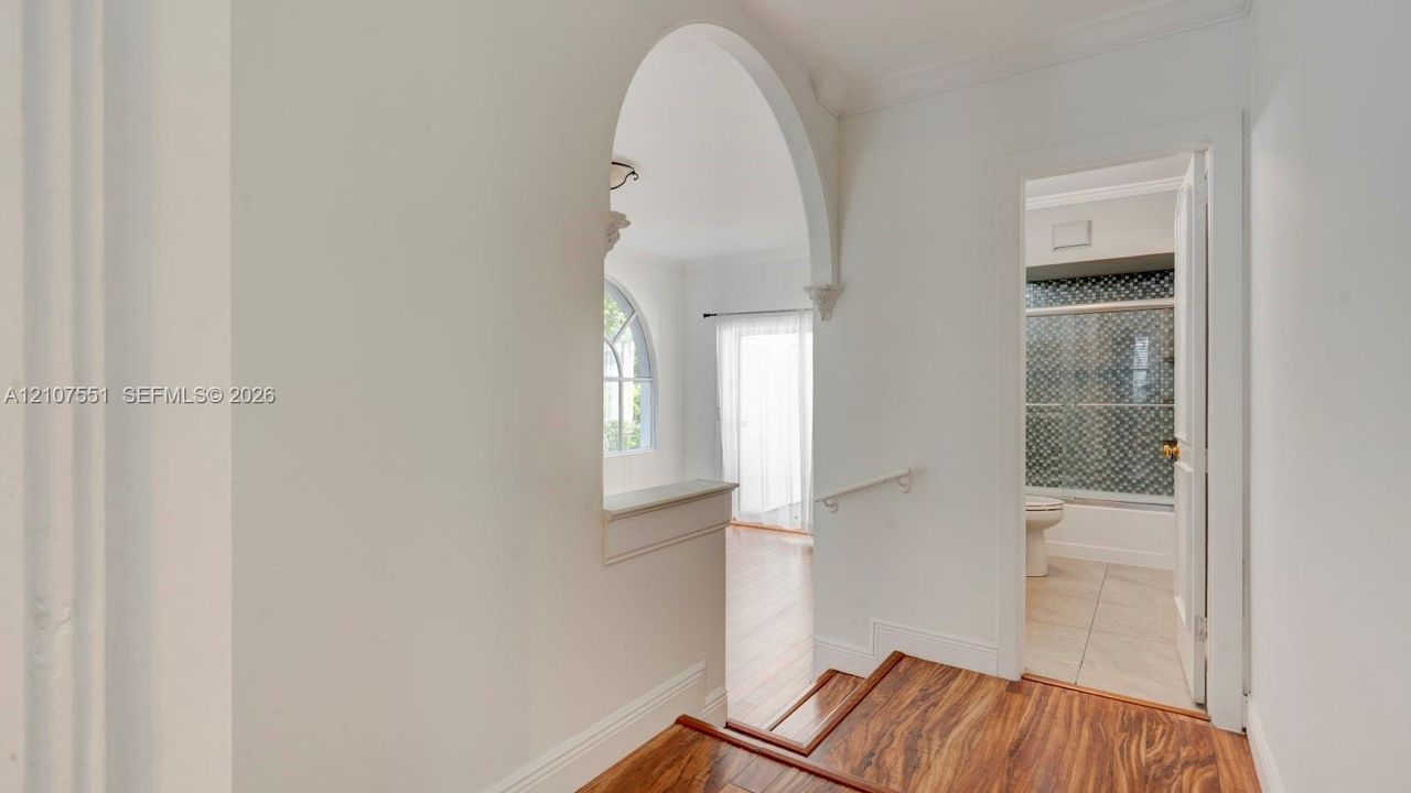 Interior featuring a structural arched opening, wood-finish flooring, and crown molding