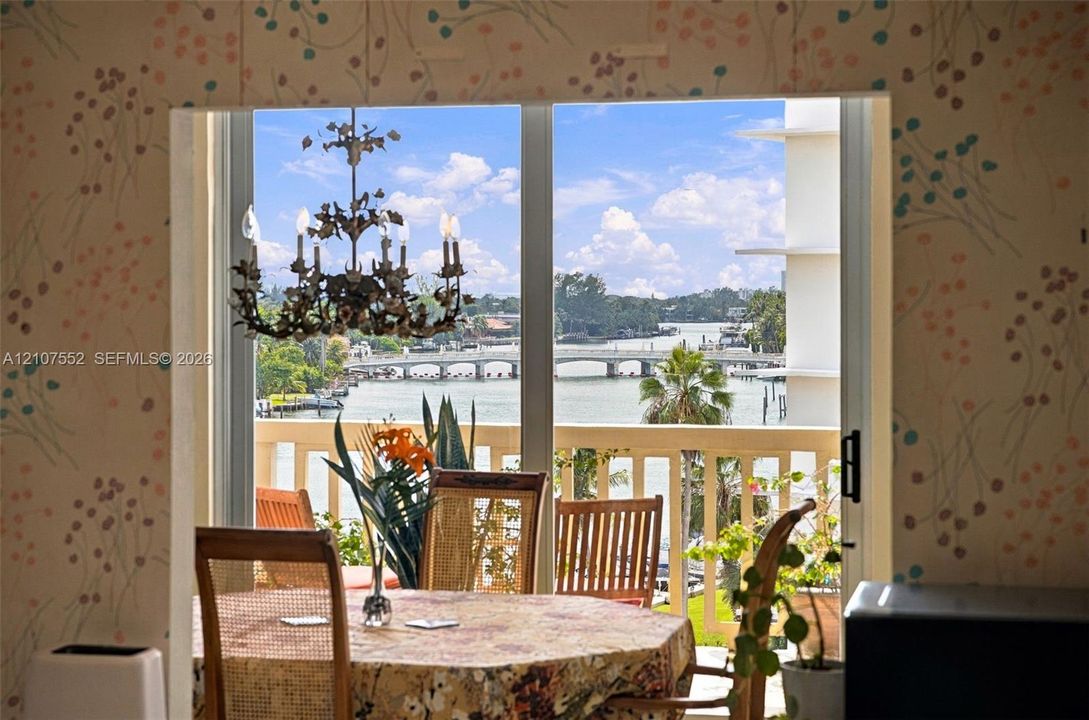 Floor-to-ceiling sliding glass door, decorative metal chandelier, and exterior balcony featuring a balustrade railing with water and bridge scenery