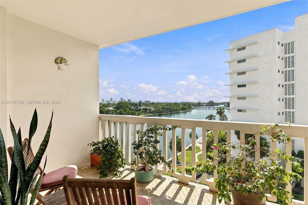 Covered balcony with a concrete balustrade and tile flooring, featuring expansive water and skyline scenery