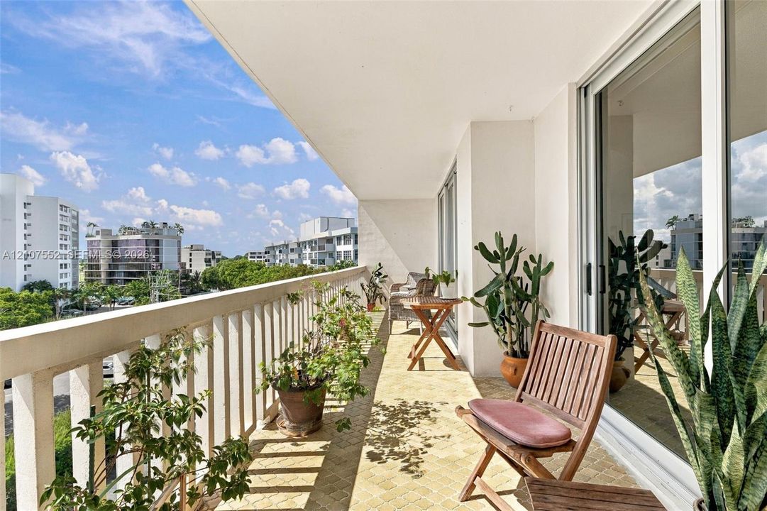 Covered balcony featuring patterned tile flooring, white vertical railings, and large sliding glass doors