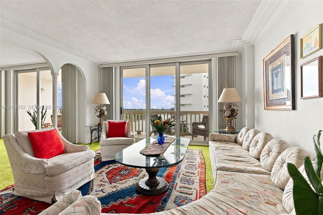 Living area featuring expansive floor-to-ceiling glass sliding doors, ornate arched architectural detailing, crown molding, and a private balcony