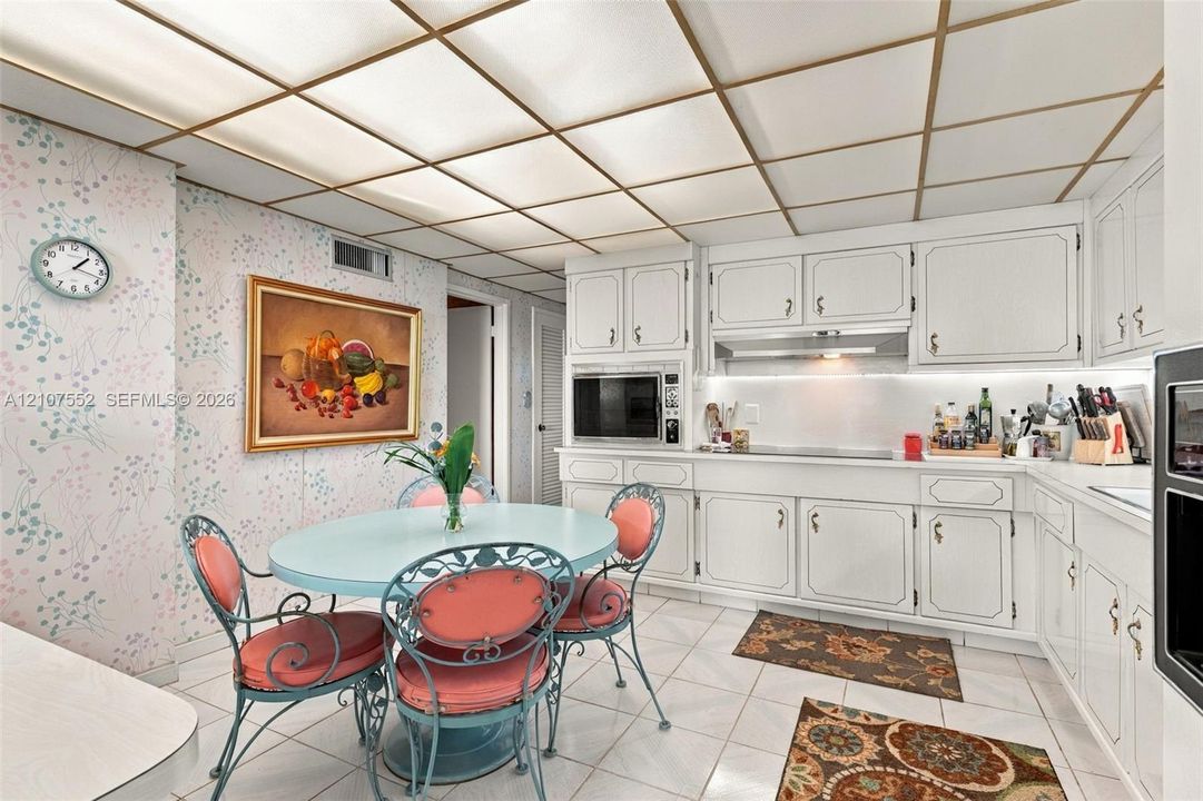 Kitchen featuring white cabinetry, integrated stainless steel appliances, ceramic tile flooring, and a grid-style drop ceiling