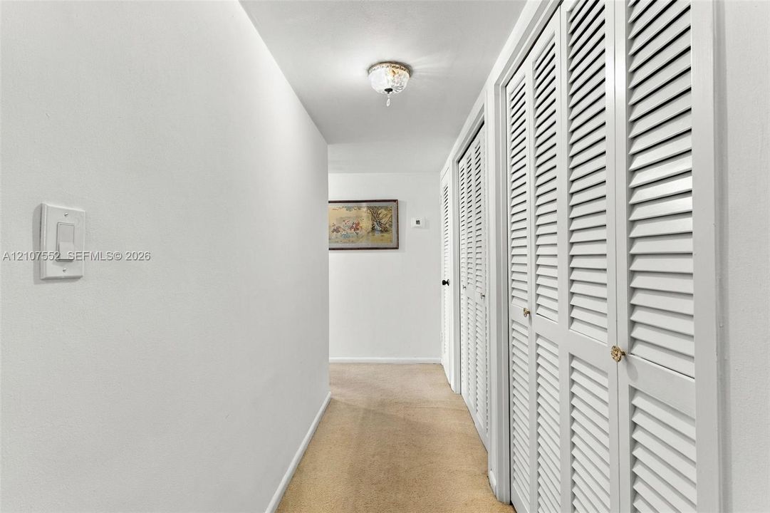 Hallway to 3 huge bedrooms featuring white walls, carpeted flooring, and multiple sets of white louvered-style closet doors