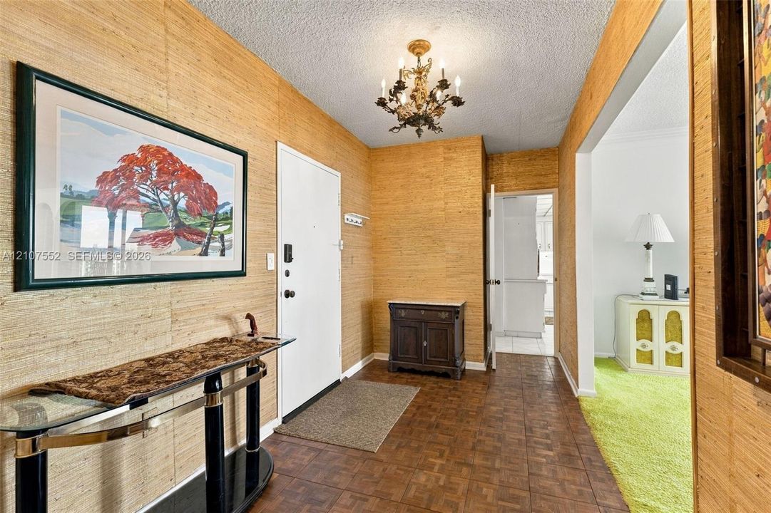 Foyer featuring textured wall coverings, parquet flooring, and an ornamental multi-arm ceiling chandelier