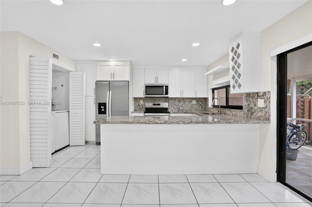 Kitchen featuring white cabinetry, stone countertops, stainless steel appliances, built-in wine storage, and ceramic tile flooring