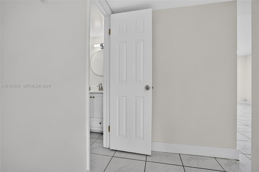 Six-panel interior door with brushed nickel hardware, leading to a vanity area featuring a round mirror, integrated sink, and polished chrome faucet