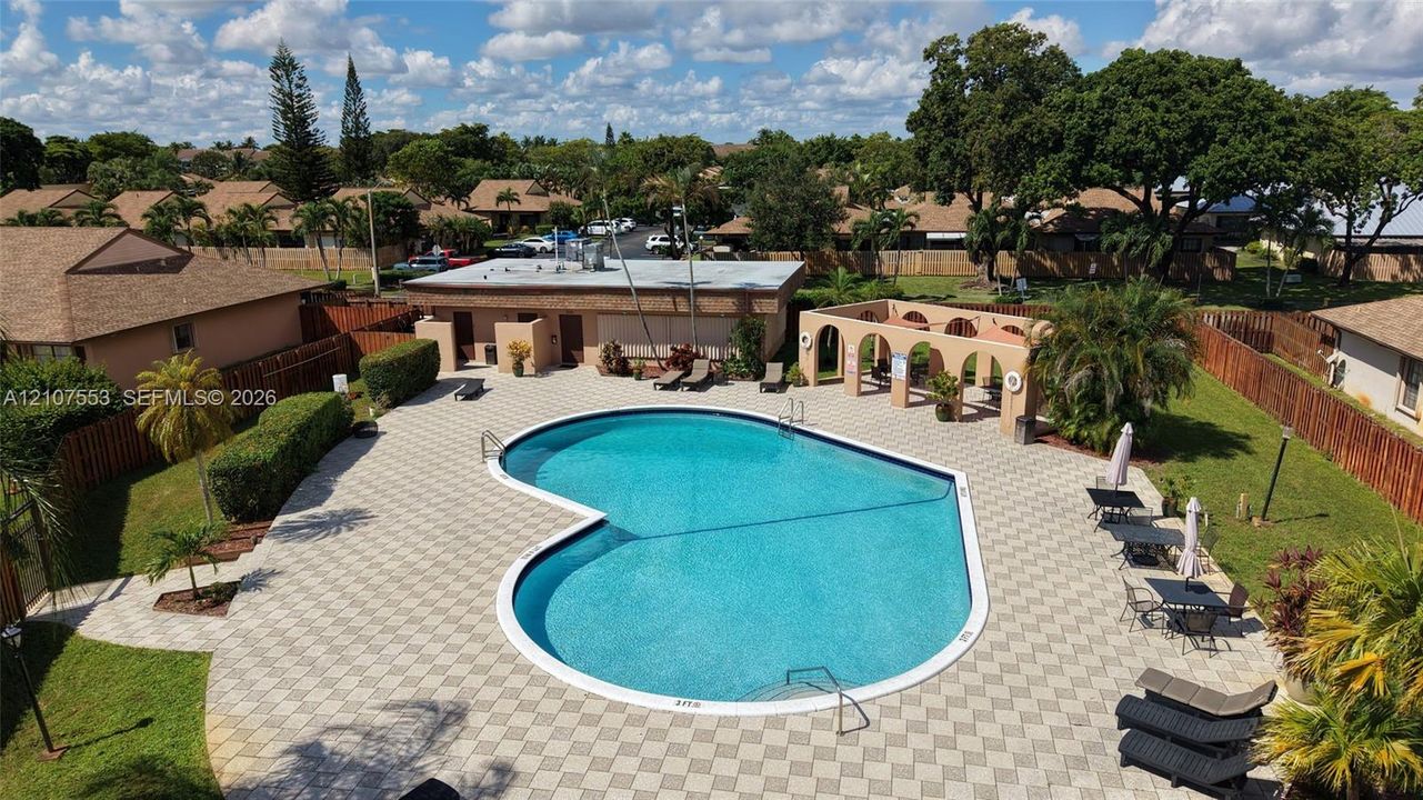 Community pool featuring an expansive paved deck, covered seating pavilion with arched masonry, and manicured green space