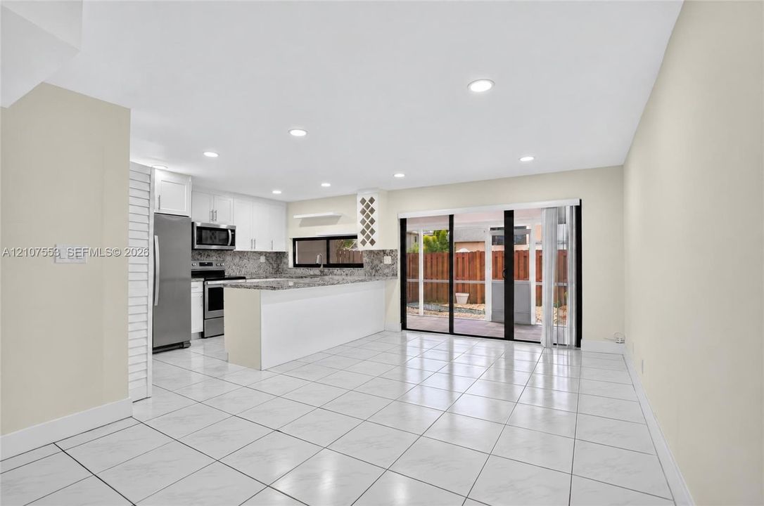Open-concept kitchen featuring a breakfast bar, stone-finish countertops, stainless steel appliances, recessed lighting, and tile flooring