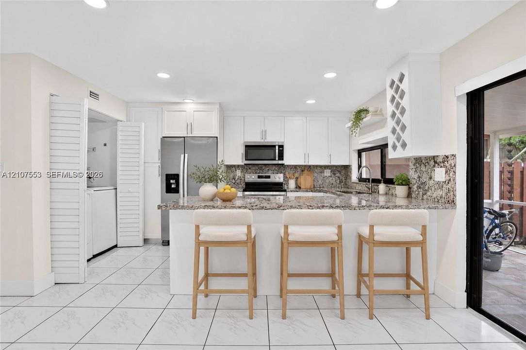 Kitchen featuring white shaker-style cabinetry, stone-finish countertops, stainless steel appliances, a built-in wine rack, and tile flooring