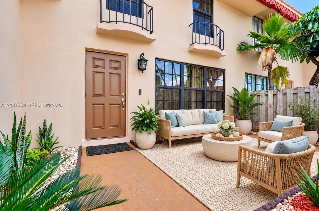 Stucco exterior featuring dual upper-level metal balconies, a multi-pane grid window, six-panel entry door, and a paved courtyard