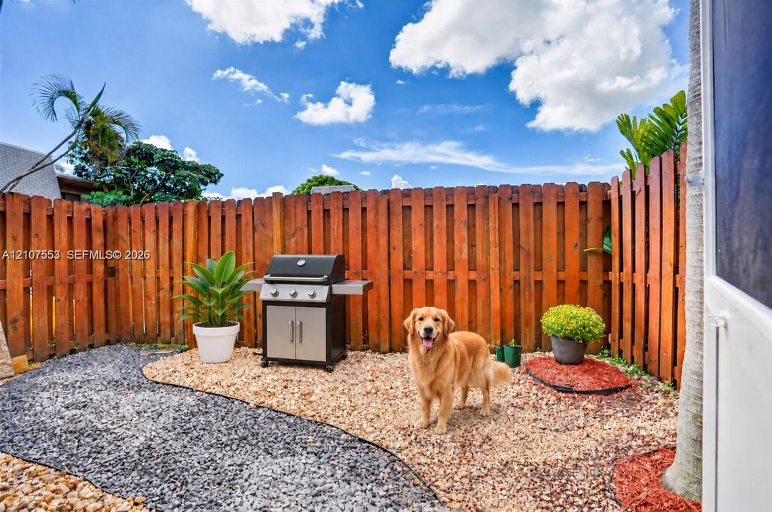 Private courtyard featuring a high wood privacy fence, decorative gravel landscaping, and a built-in outdoor cooking station