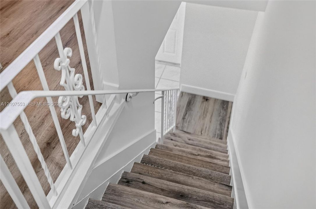 Staircase featuring wood-finish flooring, white metal balusters with decorative scrollwork, and a matching handrail