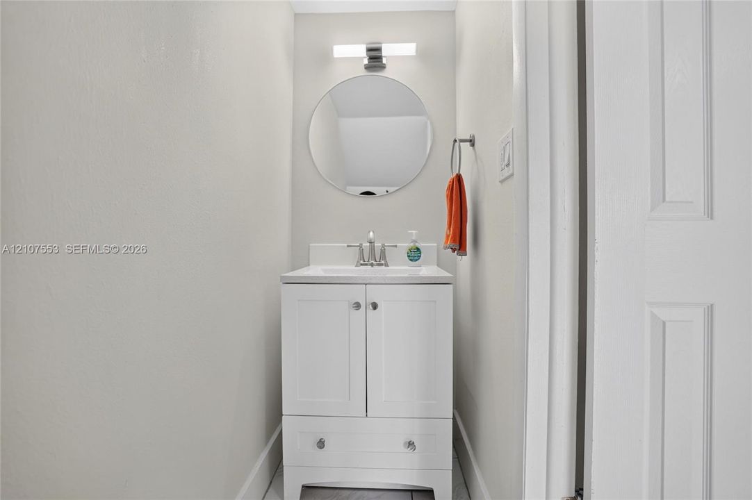 White vanity with lower storage drawer, integrated basin, brushed nickel hardware, circular wall-mounted mirror, and horizontal LED light fixture