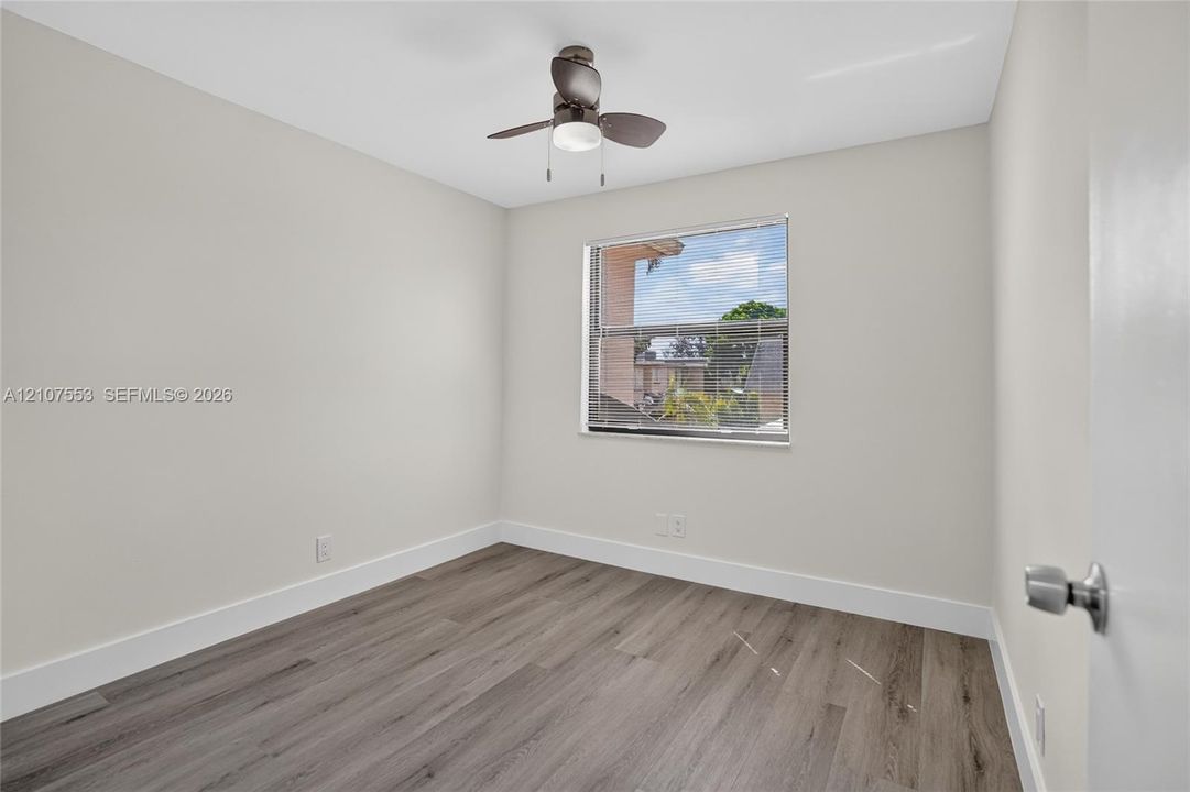 Neutral-toned interior room featuring wood-finish flooring, a ceiling fan with integrated light fixture, and a window with horizontal blinds