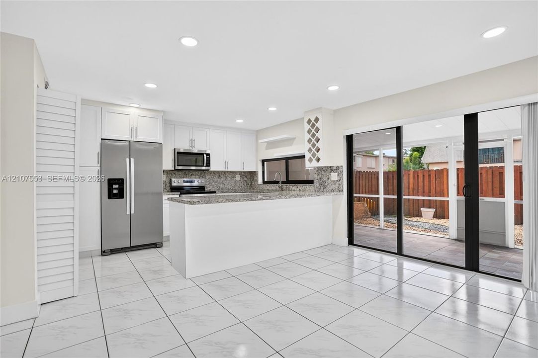 Kitchen featuring white cabinetry, stone-finish countertops, stainless steel appliances, built-in wine rack, and tile flooring throughout