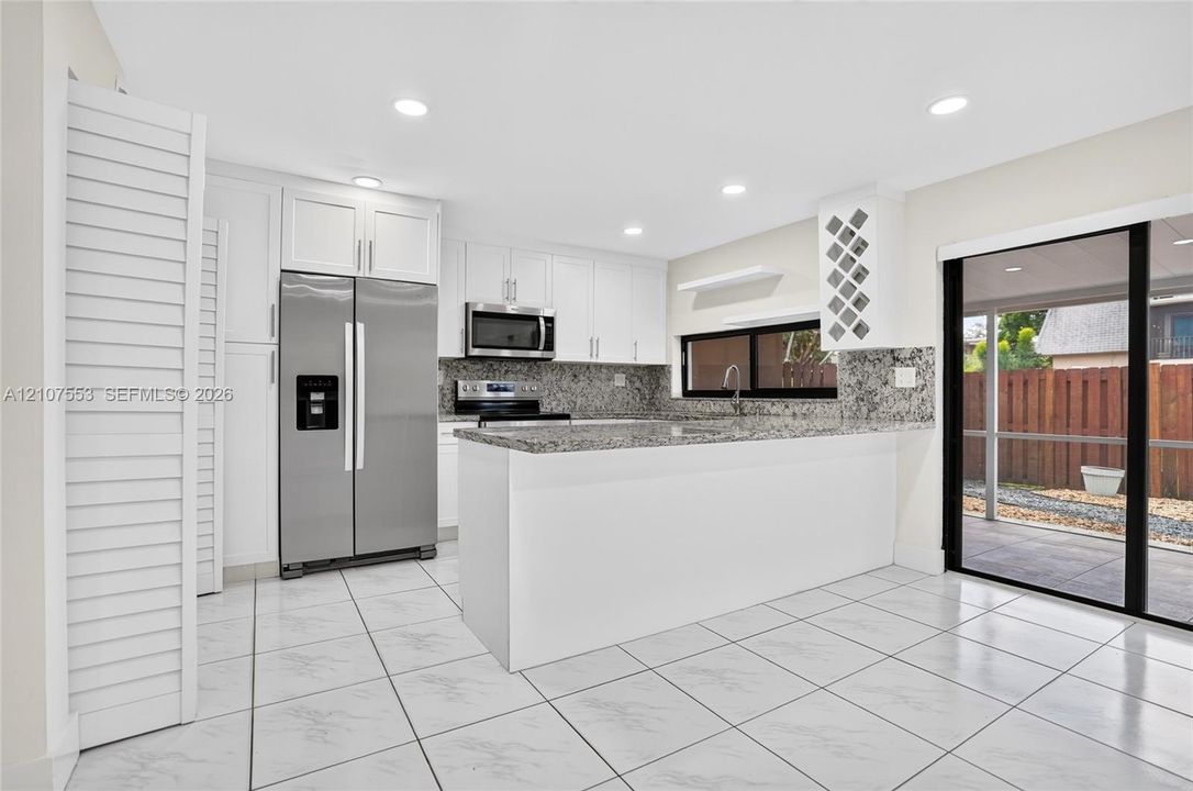 Kitchen featuring white cabinetry, stone countertops, stainless steel appliances, a built-in wine rack, and tile flooring